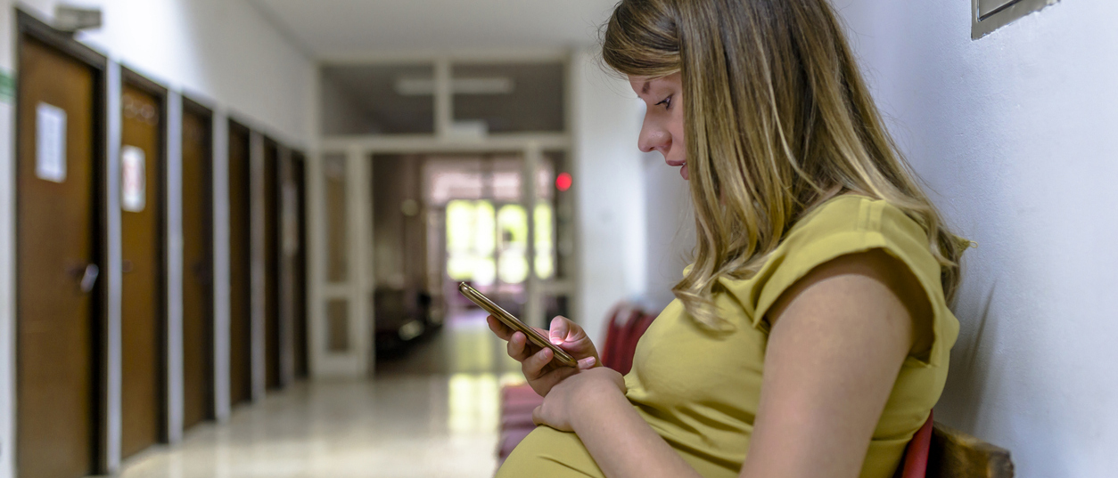 Pregnant woman using mobile phone in corridor